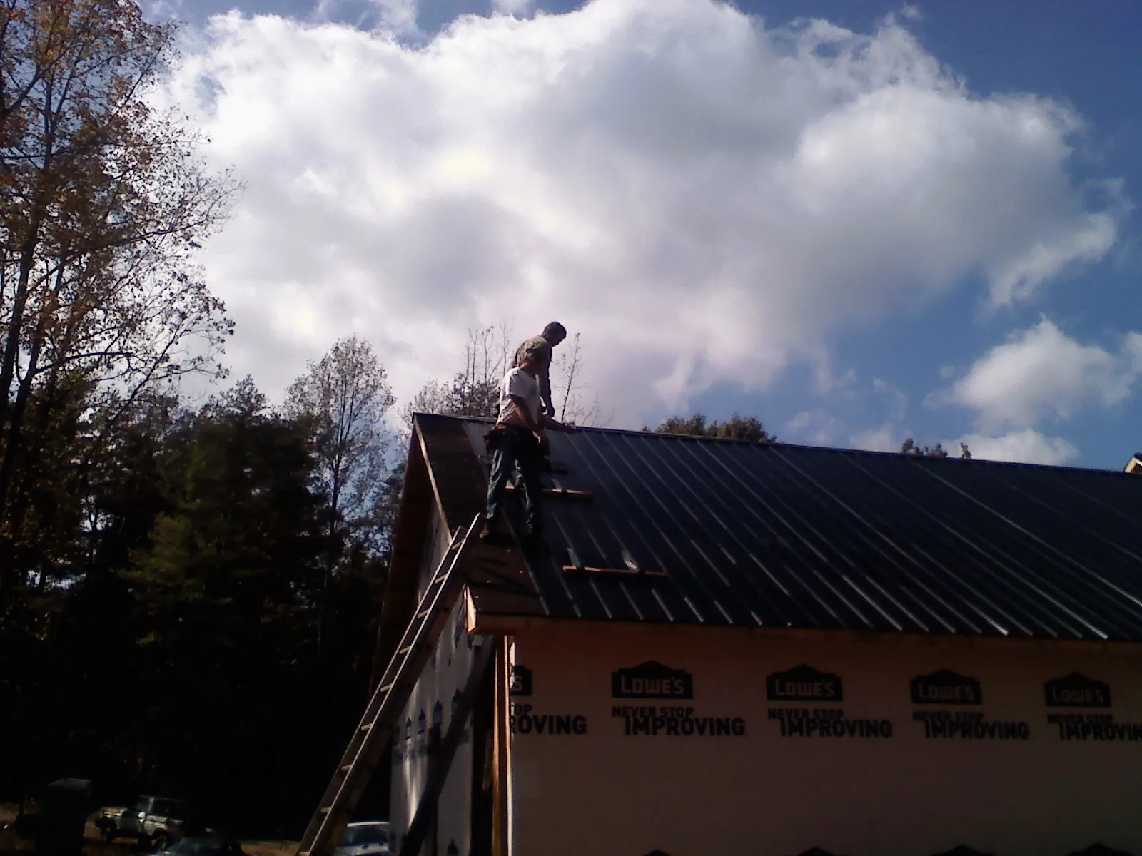 Roofer fastening dark metal panels high against a cloudy sky, from a Roof Inspection job in Matthews