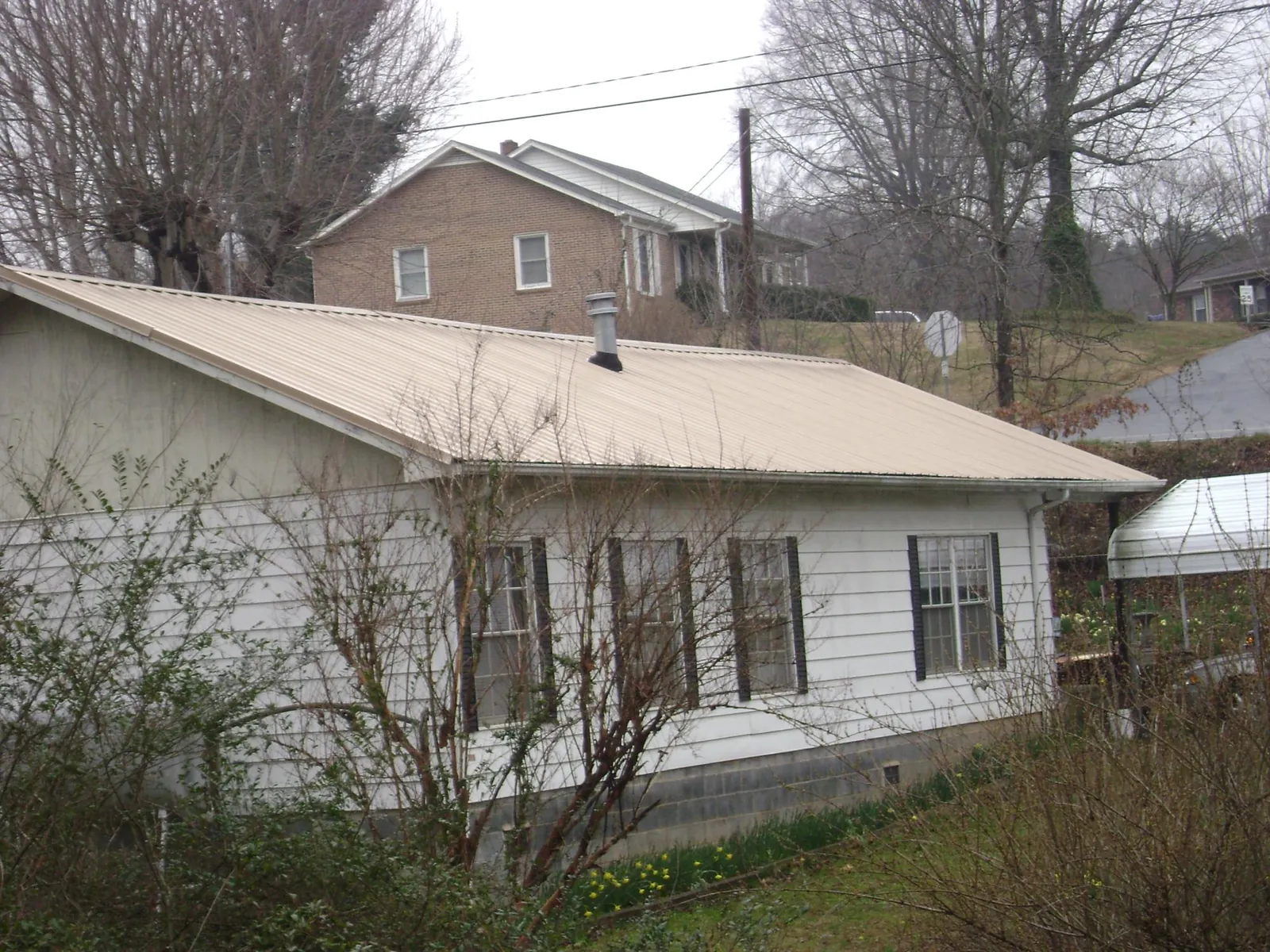 Tan metal roof on a white sided house set into a hillside — Commercial Roofing by Roofing Brothers in Matthews