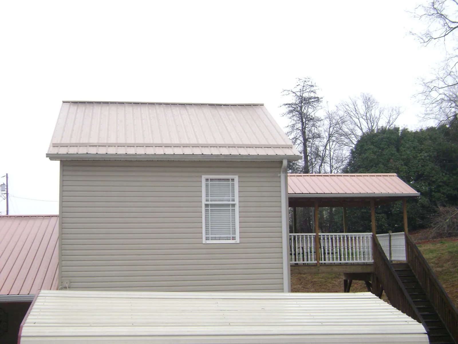 Tan metal roofs on a two story addition and attached porch, from a Roof Replacement job in Matthews
